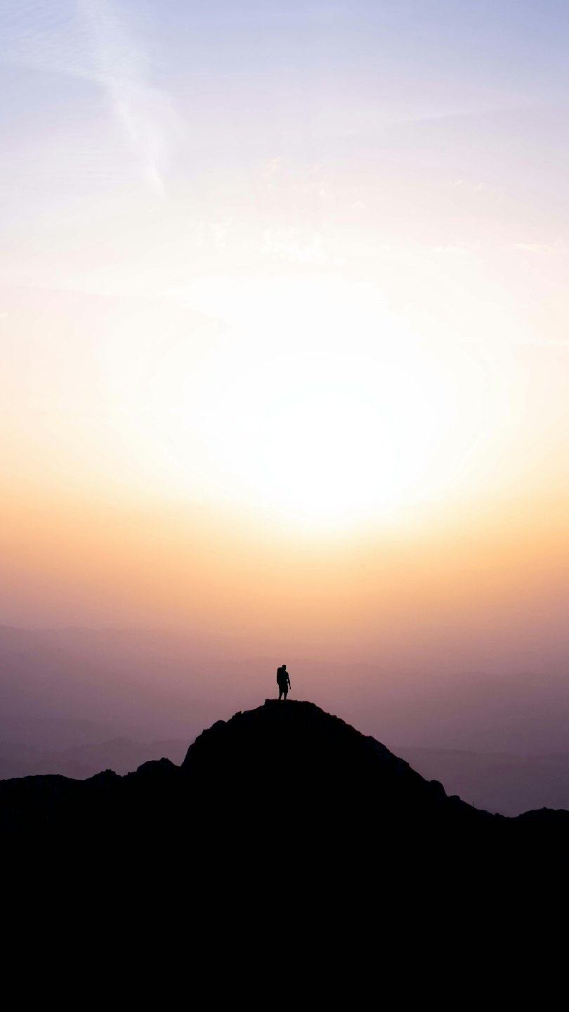 Backpacker silhouetted on mountain peak at sunrise.