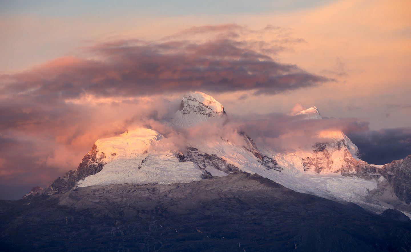 Snow-capped mountains at sunset with dramatic clouds.