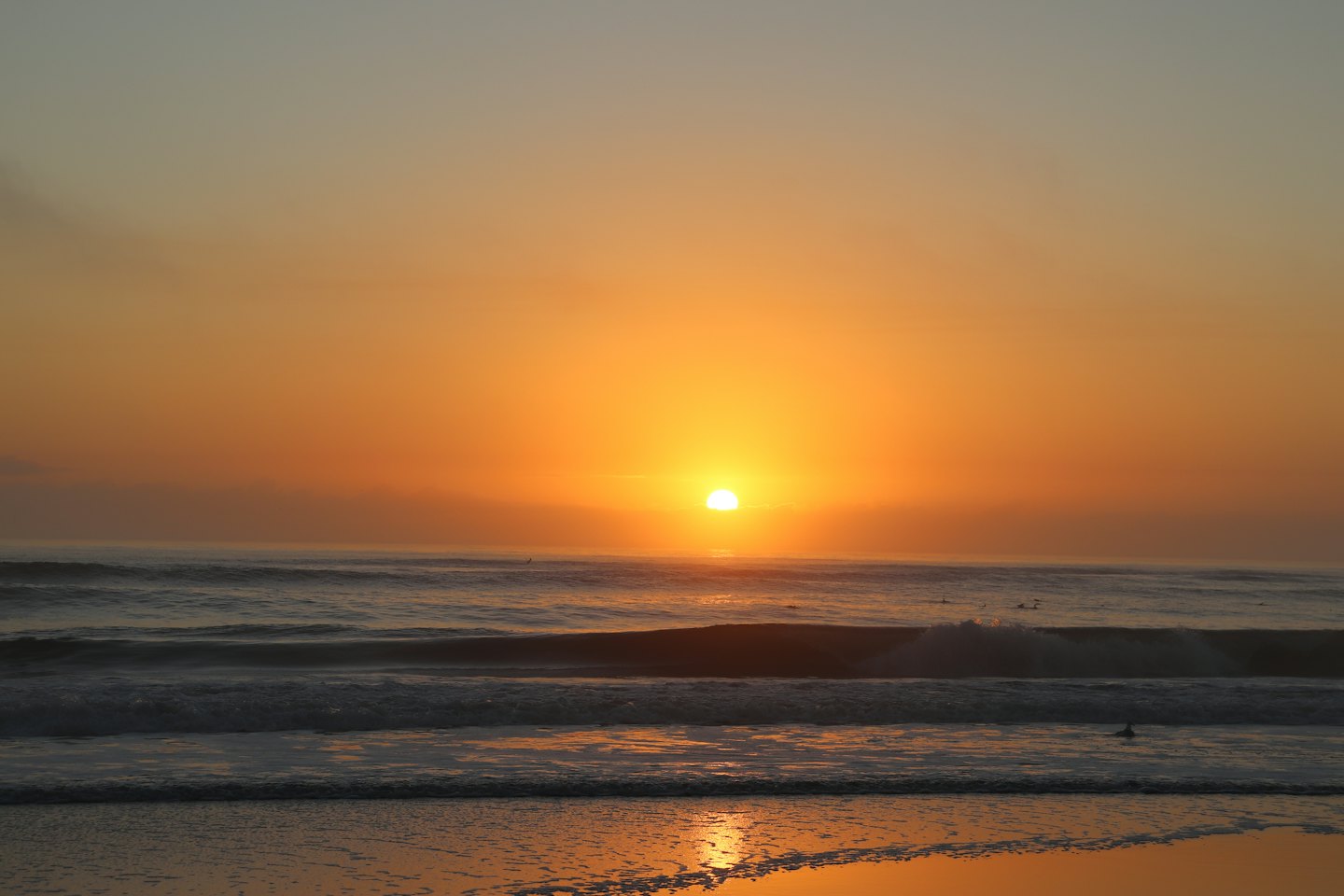 Waves roll onto a sandy beach during a golden sunset.