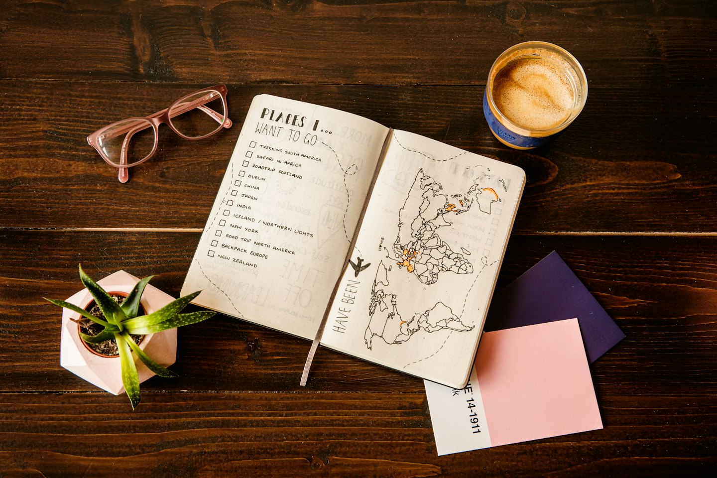 Notebook with travel plans and world map on a wooden desk.